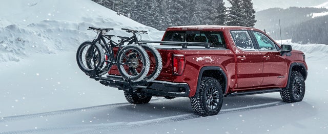 Red GMC Sierra 1500 with an attached bike rack driving through the snow
