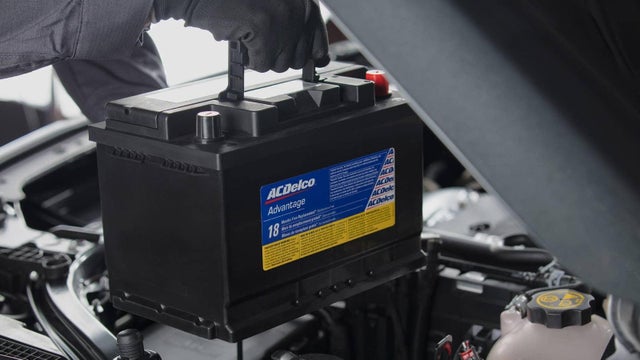 An automotive battery being installed under an open hood