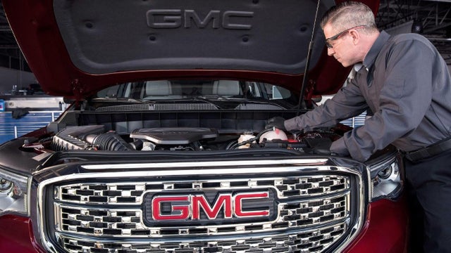 A service technician working under the hood a GMC vehicle