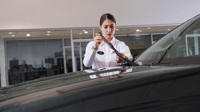 A certified service professional inspecting a wiper blade on a vehicle
