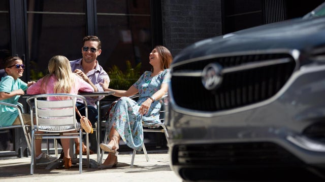 A smiling family at a table outdoors with a Buick vehicle grille blurred in the foreground | Junction Buick GMC in Chardon OH