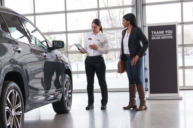 A service representative speaking with woman next to a vehicle in a service center