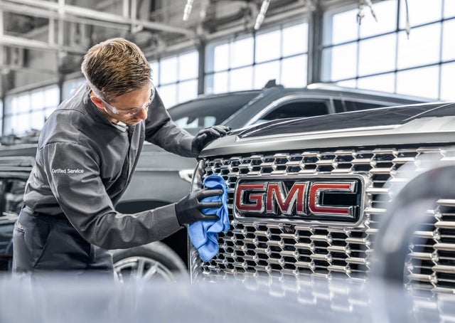 A service technician cleaning the grille of a GMC vehicle
