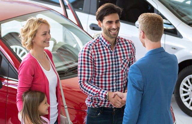 A man with woman and child, shaking the hand of a sales person in an automobile showroom
