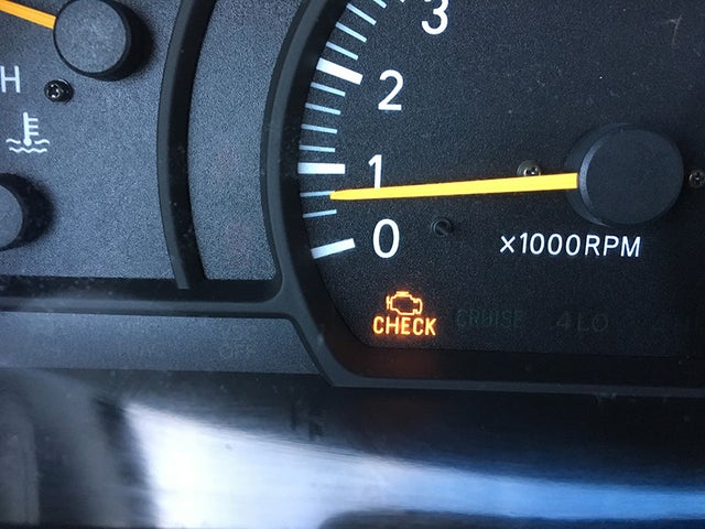 A vehicle dashboard with the check engine indicator light turned on
